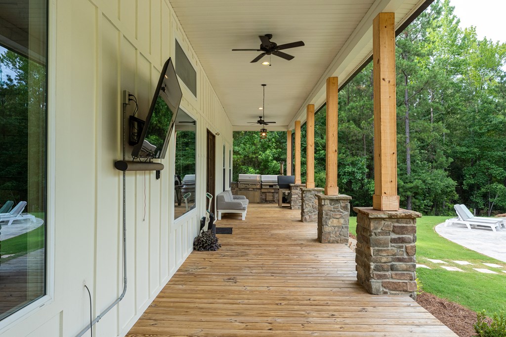 Covered wooden porch with stone-based posts, ceiling fans, seating, and a wooded lawn.