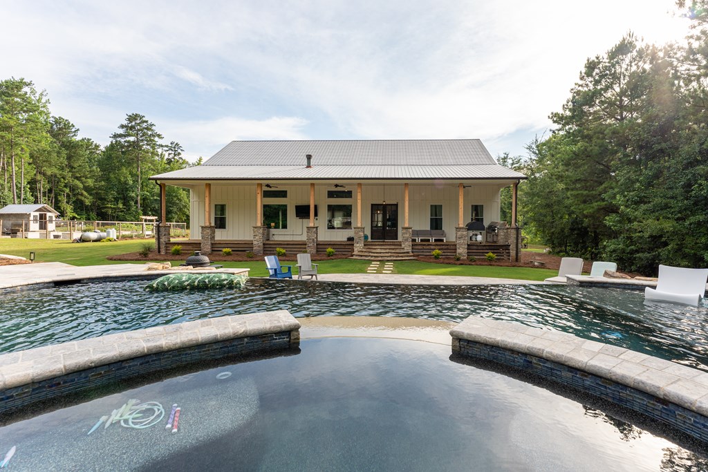 Single-story home with a covered porch beyond a large stone-edged swimming pool.