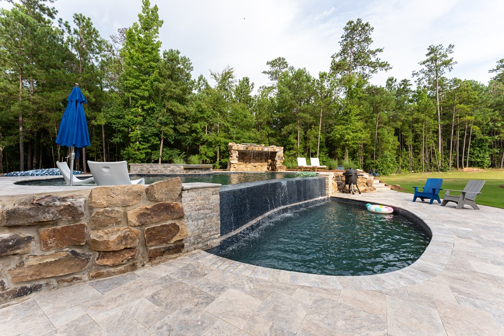 Outdoor pool with a curved stone edge, raised waterfall, and wooded backdrop.
