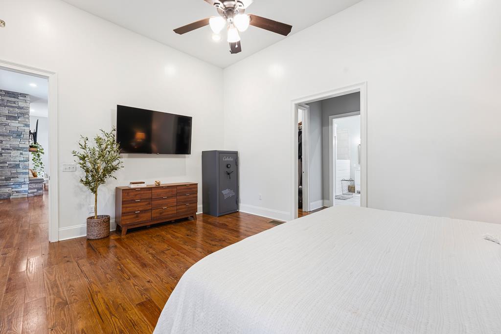 Bedroom with a white bed, hardwood floors, and a wall-mounted television.