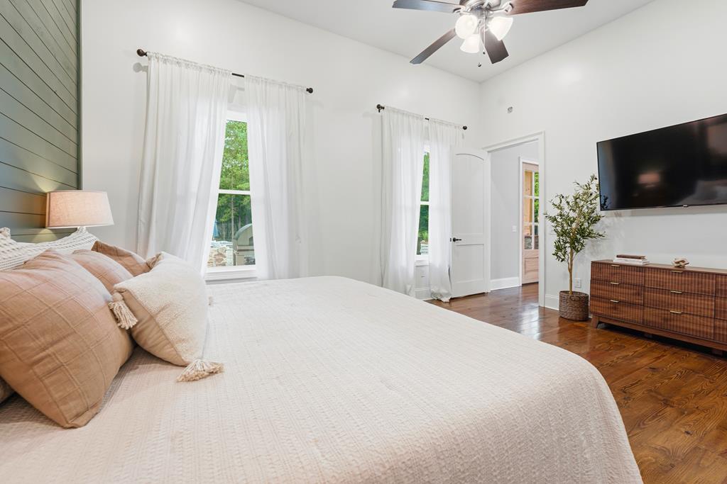 Furnished bedroom with a sage-green shiplap accent wall, hardwood floors, and a wall-mounted television.