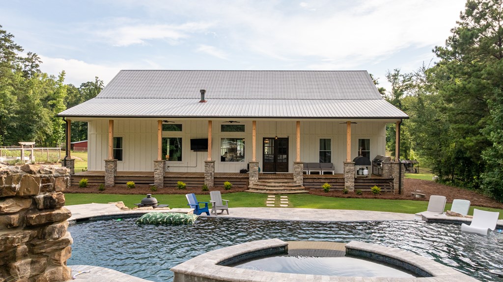 House with a broad covered porch behind a swimming pool and raised circular spa.