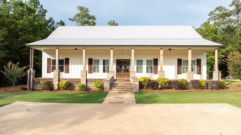 White single-story house with a broad covered porch, stone columns, and a paved driveway.