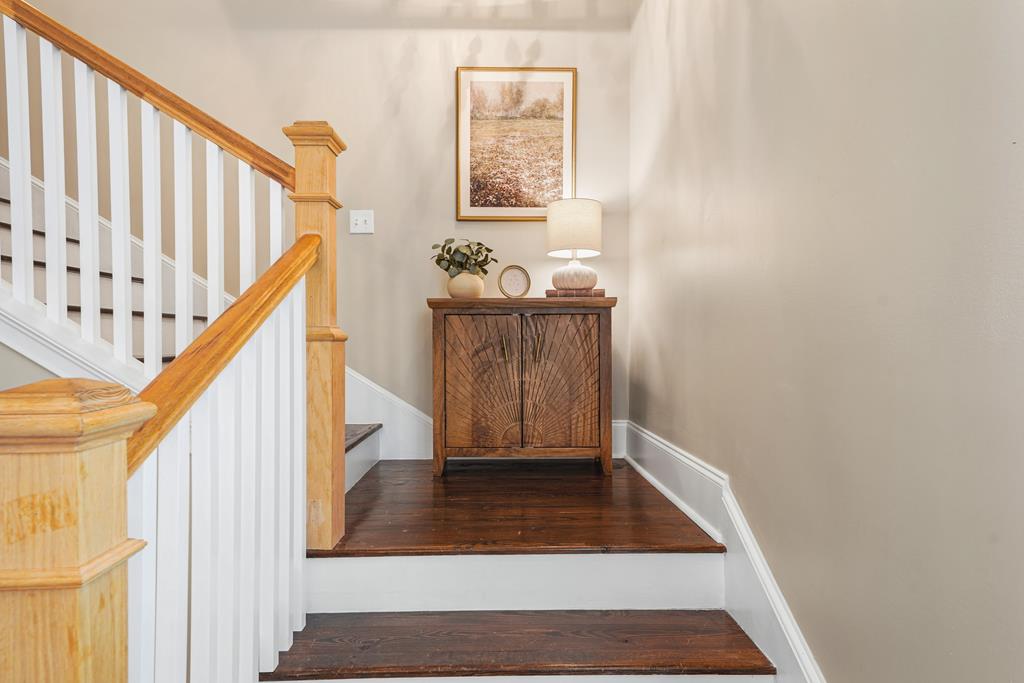 Staircase landing with a wood handrail, white balusters, hardwood floors, and a console table.