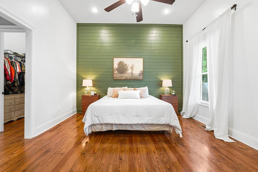 Bedroom with a green plank accent wall, hardwood floors, and an open walk-in closet.