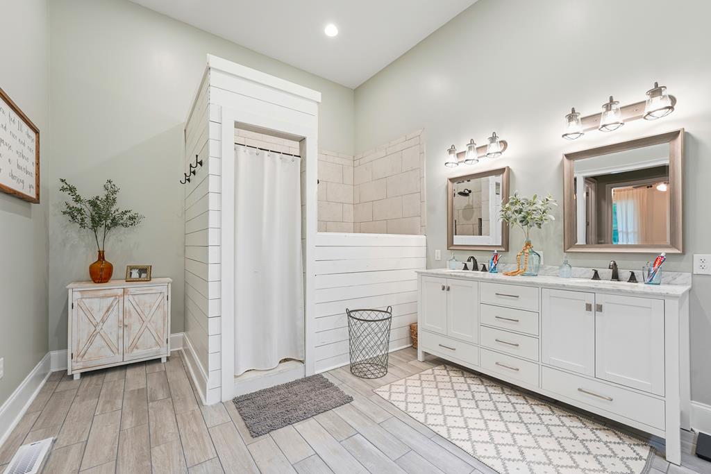 Bright bathroom with a long double vanity and tiled shower enclosure with a white curtain.