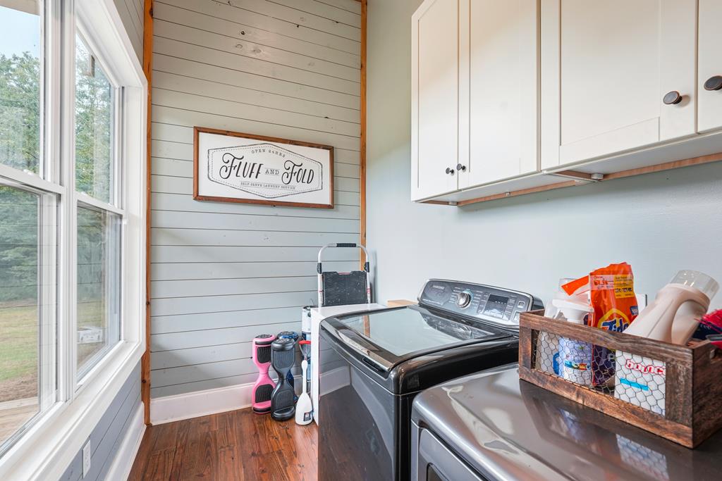 Laundry room with washer and dryer, white cabinets, large windows, and a framed “Fluff and Fold” sign.