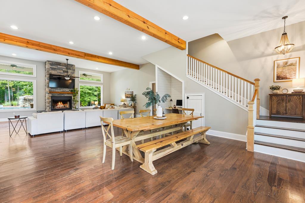 Open-plan dining and living area with exposed beams, a long farmhouse table, and a stone fireplace.