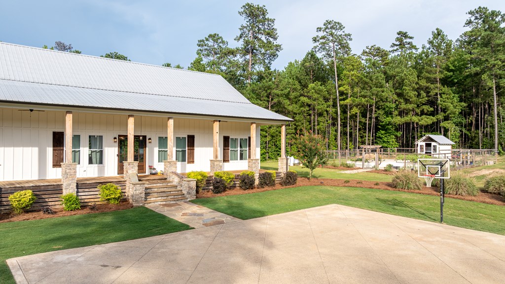 White home with a broad porch, landscaped lawn, basketball hoop, and fenced garden.