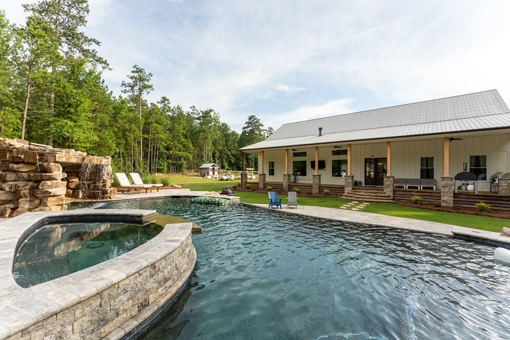 Backyard pool and raised stone spa beside a single-story home with a covered porch.