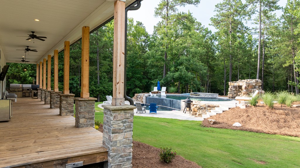 Covered wooden porch overlooking a swimming pool with a stone waterfall and wooded backdrop.