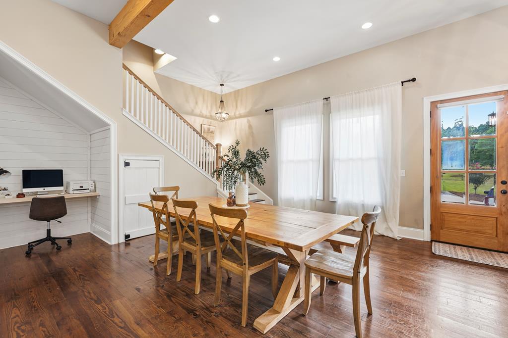 Dining area with a long wooden table, staircase, built-in desk nook, and glass exterior door.
