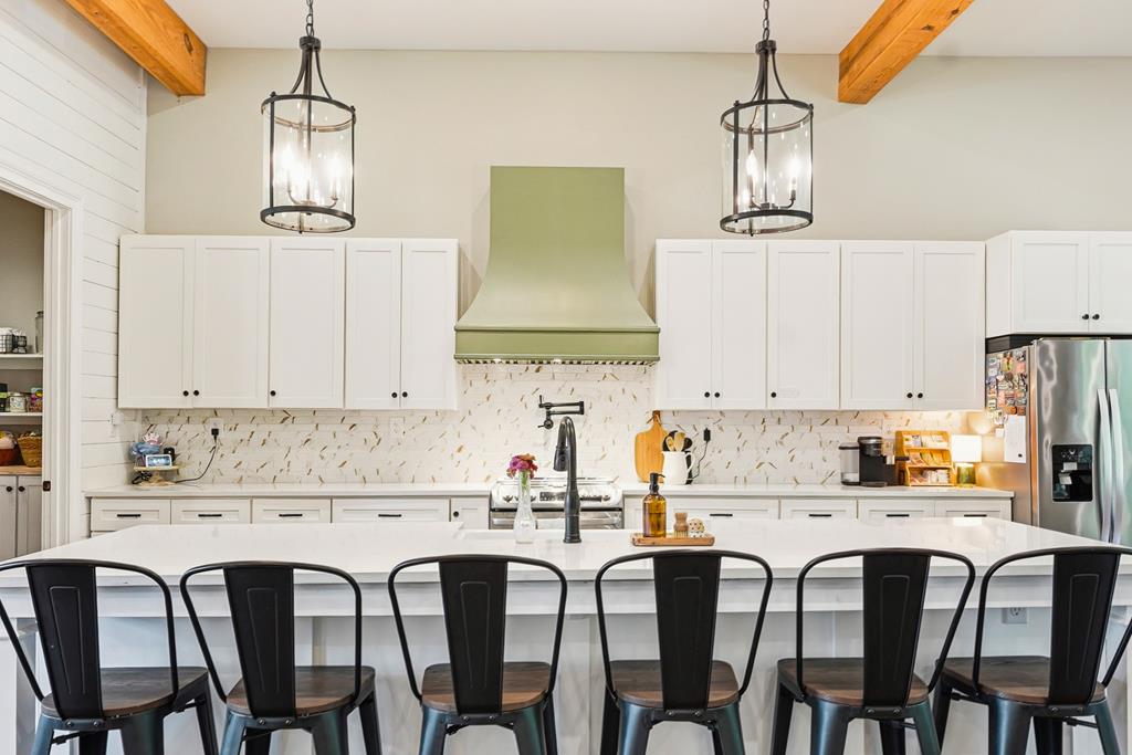 Kitchen with a large white island, black bar stools, and a pale green range hood.