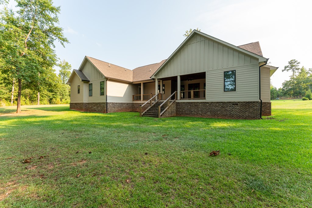 Light-colored house with a covered porch and brick foundation, set behind a broad lawn and mature trees.