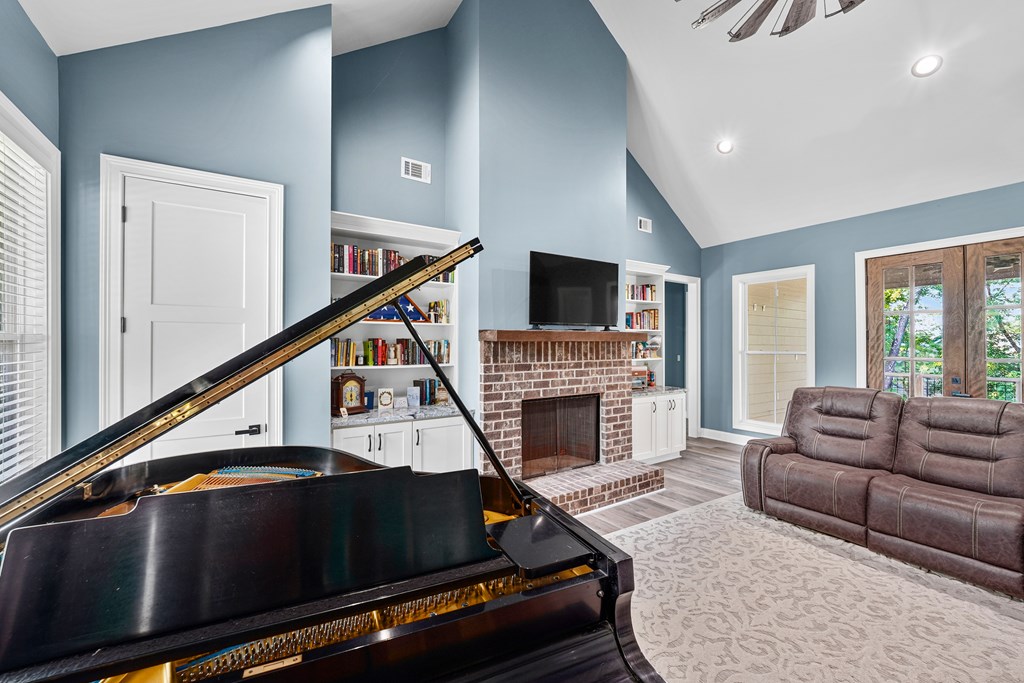 Living room with a grand piano, brick fireplace, built-in bookshelves, and brown sofa.