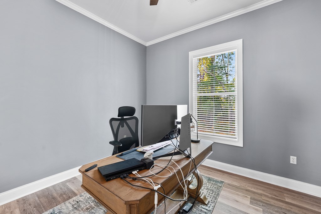 Home office with a wooden computer desk, black chair, and window with white blinds.