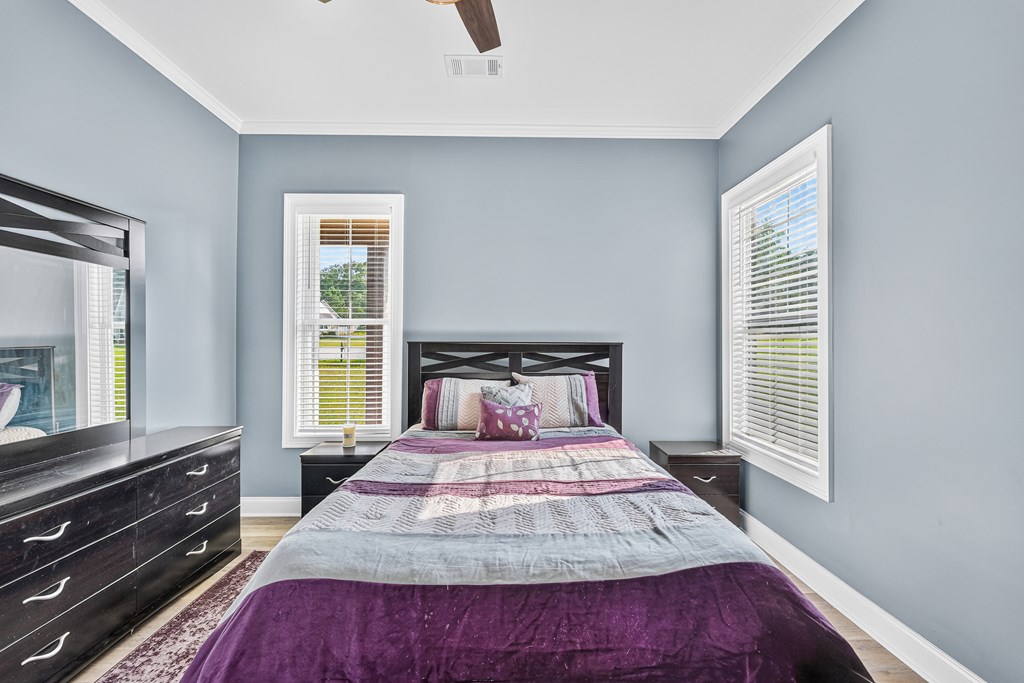Bedroom with purple and gray bedding, dark wood furniture, and two windows with white blinds.
