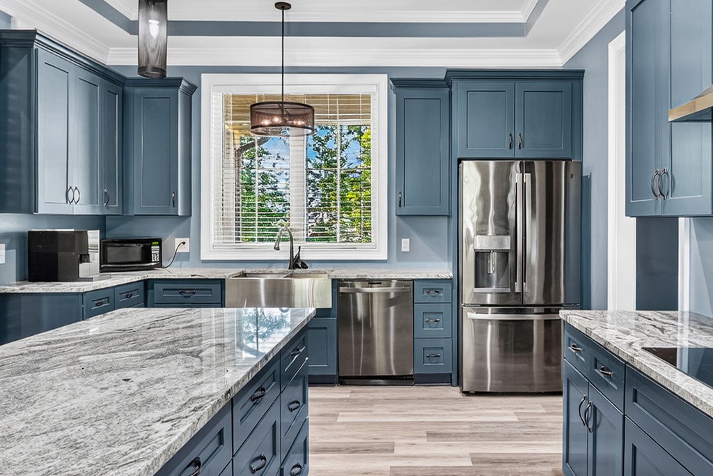 Kitchen with blue cabinets, granite counters, stainless steel appliances, and a window above the sink.