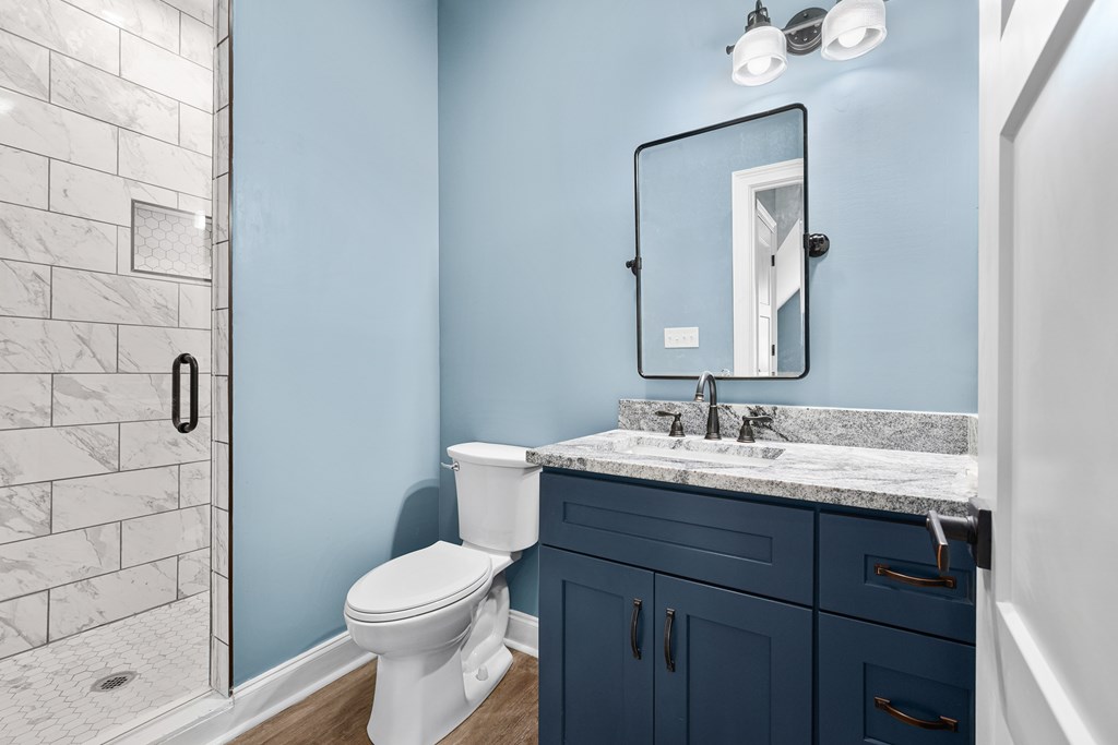 Bathroom with a marble-look tiled shower and navy vanity topped with gray stone.