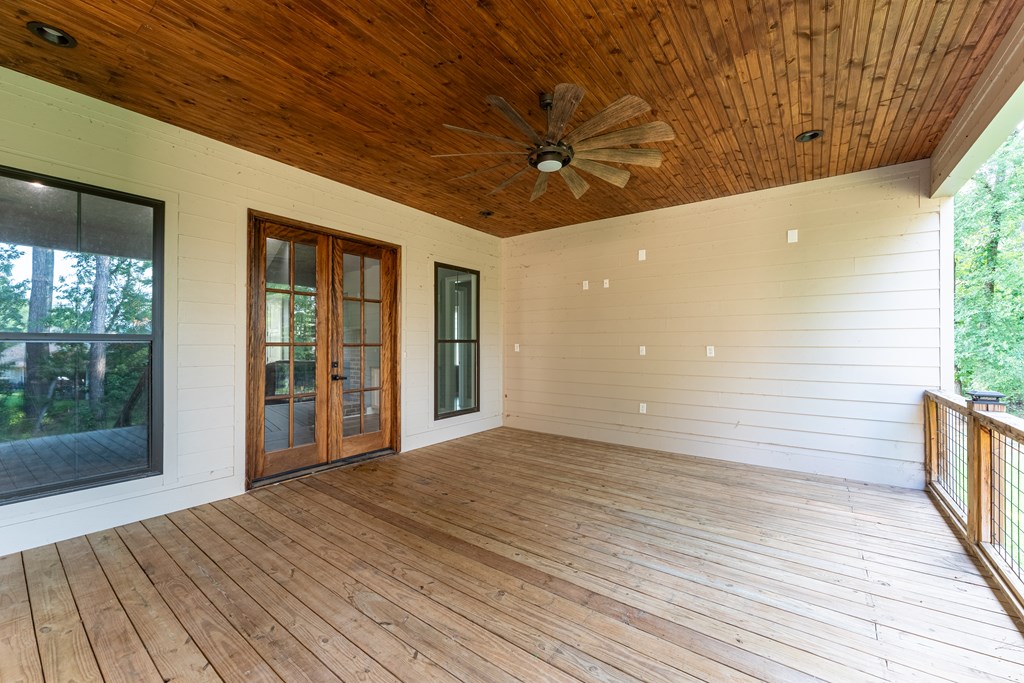 Covered porch with wood-plank floor and ceiling, ceiling fan, glass-paneled doors, and views of trees.