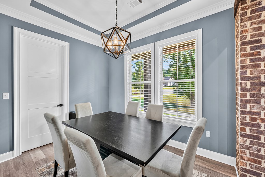 Dining room with a dark table, upholstered chairs, large windows, and an exposed brick wall.