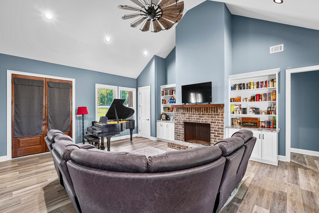 Living room with a curved gray sectional, brick fireplace, built-in bookshelves, and grand piano.