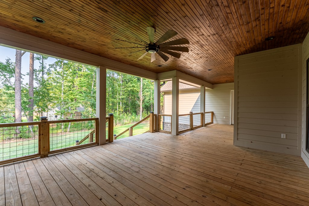 Covered wooden porch with a ceiling fan and railing overlooking a leafy yard.