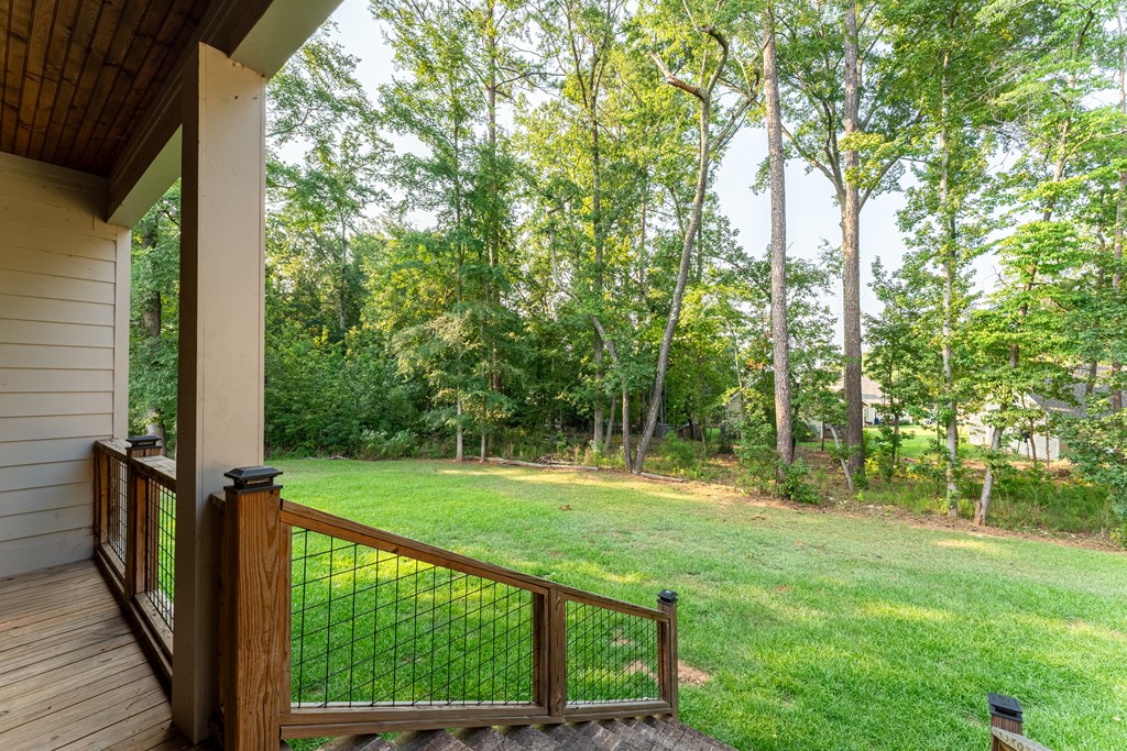 Covered wooden porch overlooking a fenced lawn and mature trees.