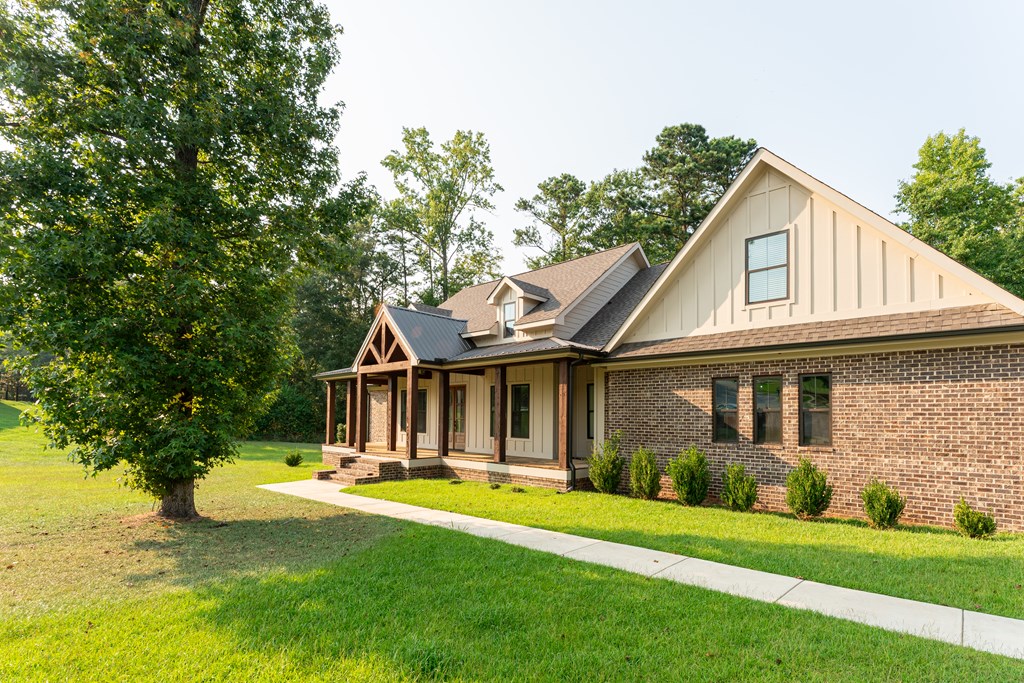 House with cream siding, brick facade, and a covered timber porch beside a broad lawn.