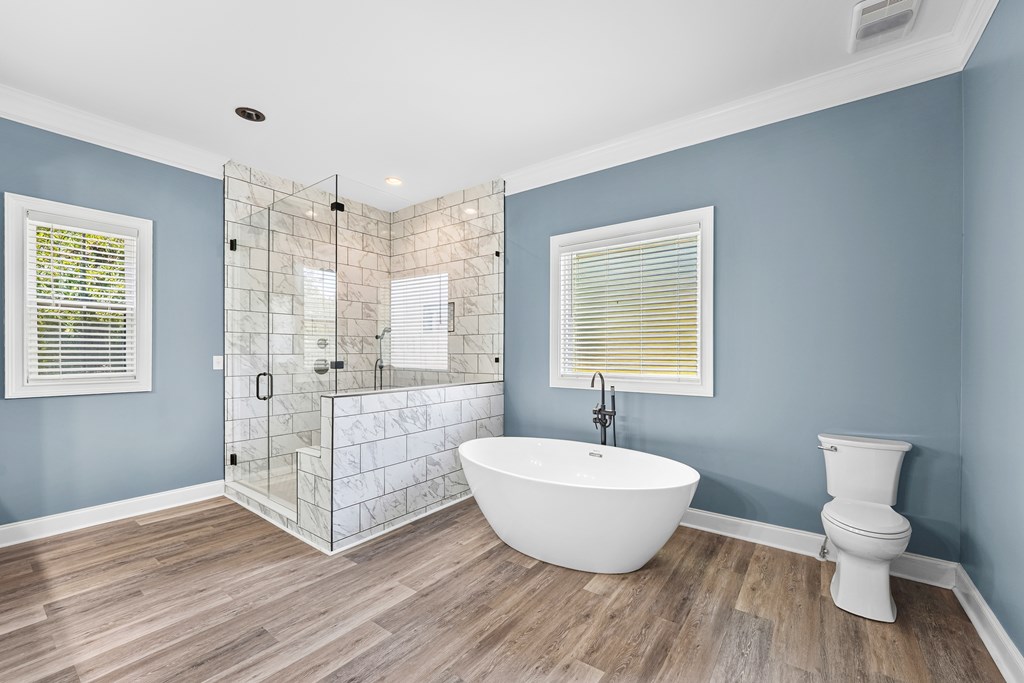 Bathroom with a freestanding tub beside a glass-enclosed marble-look tile shower.