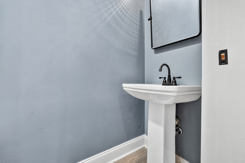 White pedestal sink with a dark faucet against gray bathroom walls.