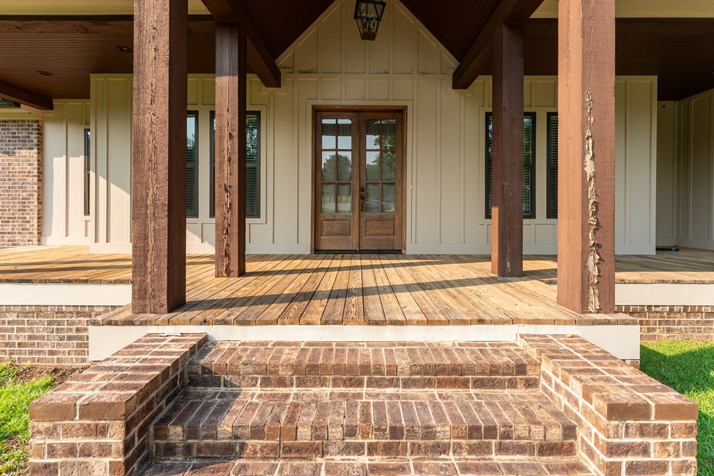 Covered wooden porch with timber posts, double entry doors, and broad brick steps.