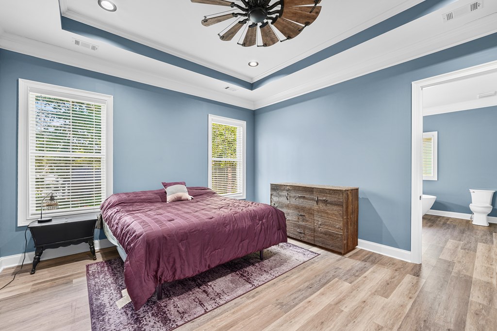 Bedroom with blue walls, a plum-covered bed, rustic dresser, and adjoining bathroom.