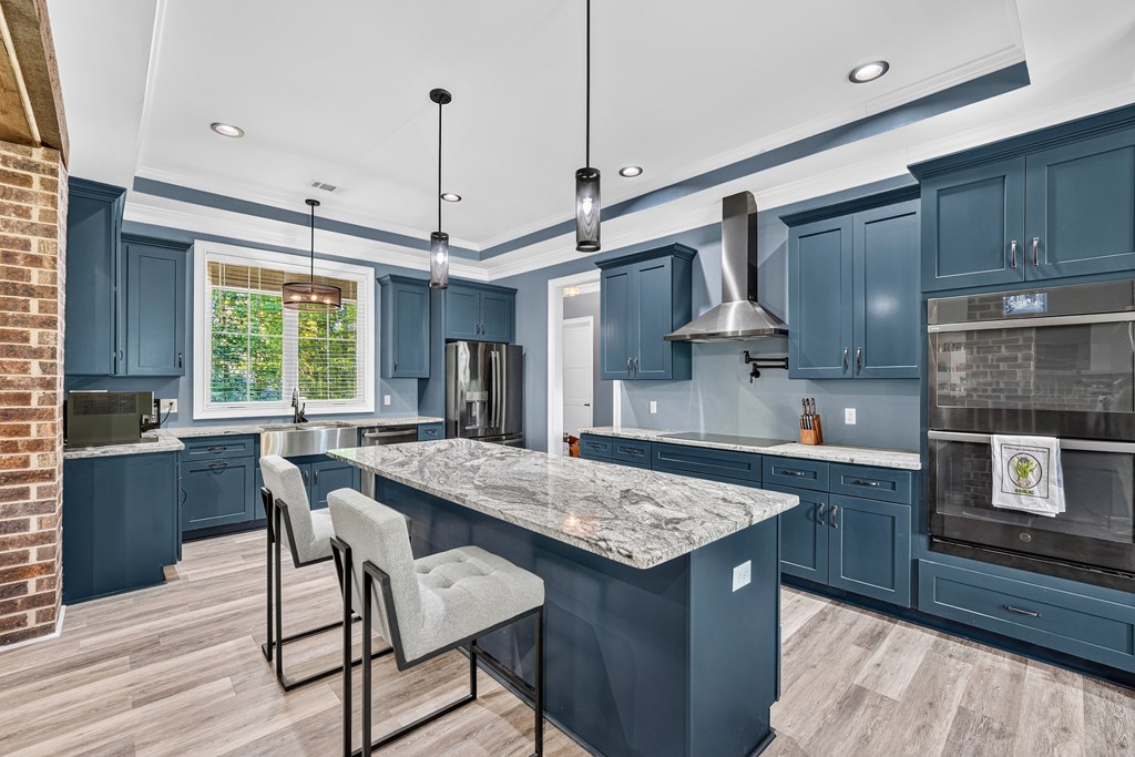 Kitchen with blue cabinets, a large veined stone island, stainless steel appliances, and two bar stools.