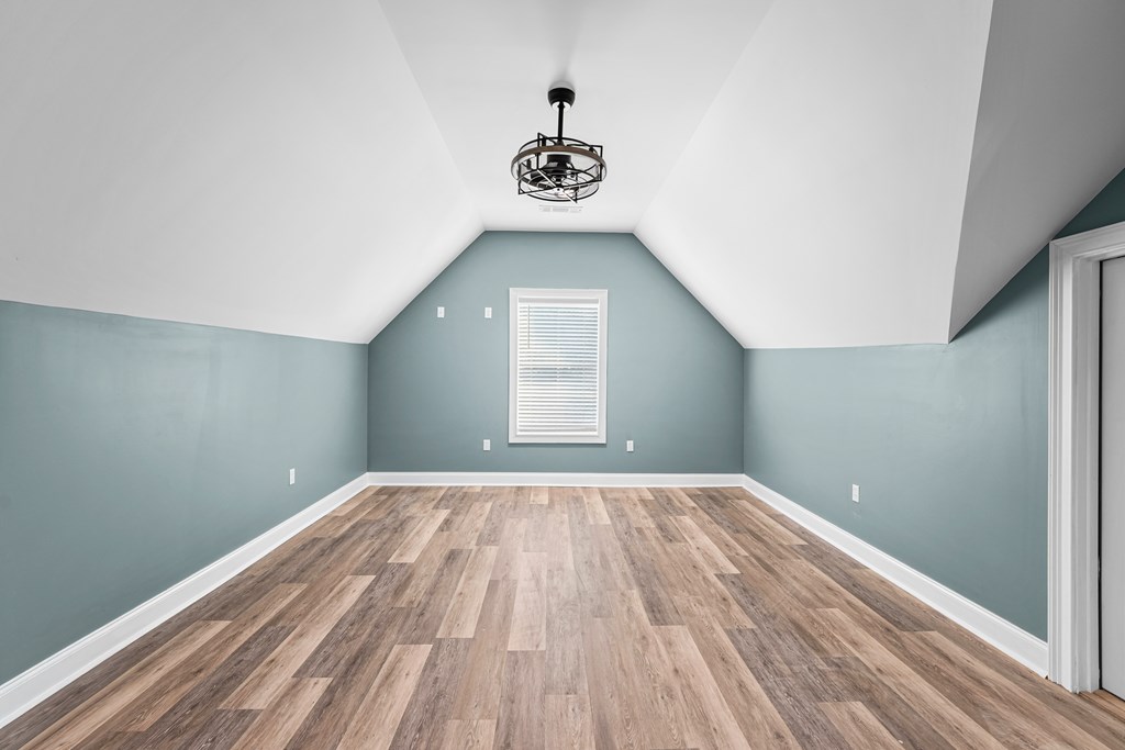 Empty room with a vaulted ceiling, blue walls, and wood-look plank flooring.