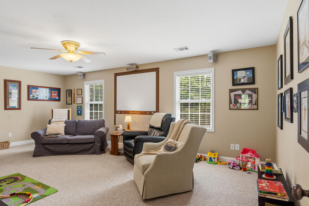 Furnished family room with a gray sofa, two armchairs, and children's toys along the wall.