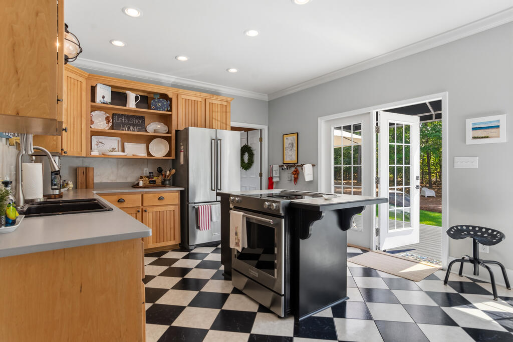 Kitchen with warm wood cabinets, checkerboard floor, central cooktop island, and open doors to a deck.