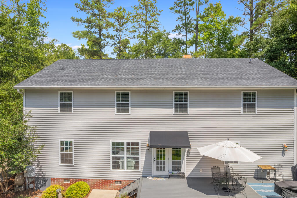 Rear of a two-story gray home with a raised deck, patio furniture, and a white umbrella.