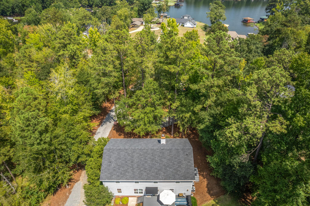 Aerial view of a house nestled among trees, with a lake visible beyond it.