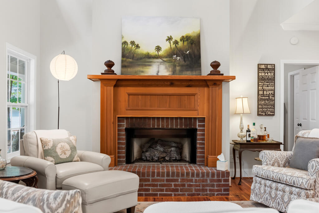 Living room with a brick fireplace, carved wood mantel, and light upholstered seating.