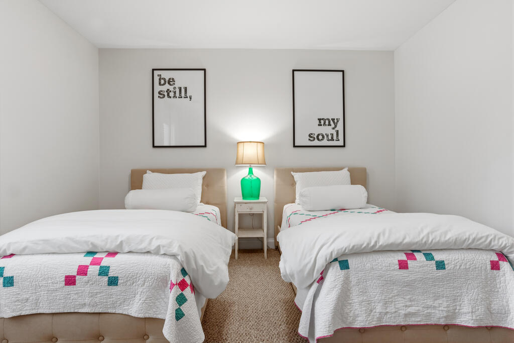 Bedroom with two twin beds, colorful geometric quilts, and a green lamp between them.