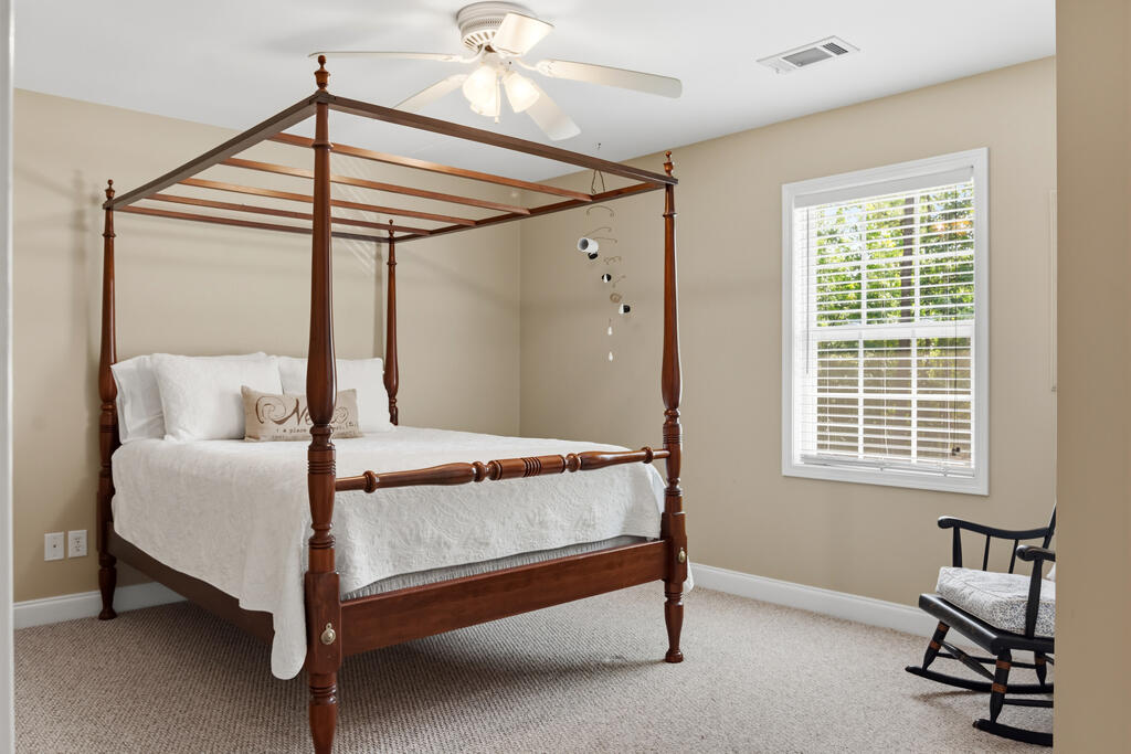 Bedroom with a dark wood four-poster bed and a rocking chair beside a bright window.