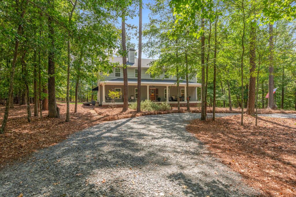 Two-story home with a covered porch at the end of a wooded gravel driveway.