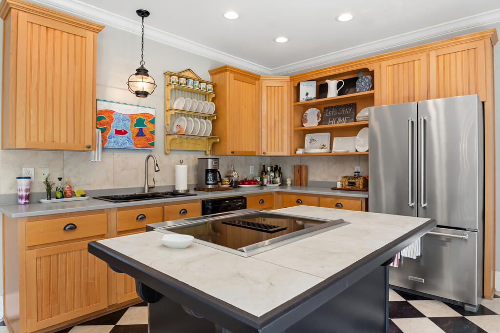 Kitchen with honey-colored wood cabinets, a large cooktop island, and a stainless steel refrigerator.