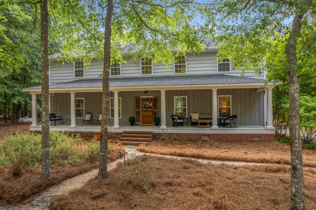 Two-story gray house with a wide columned porch and mature trees in the yard.