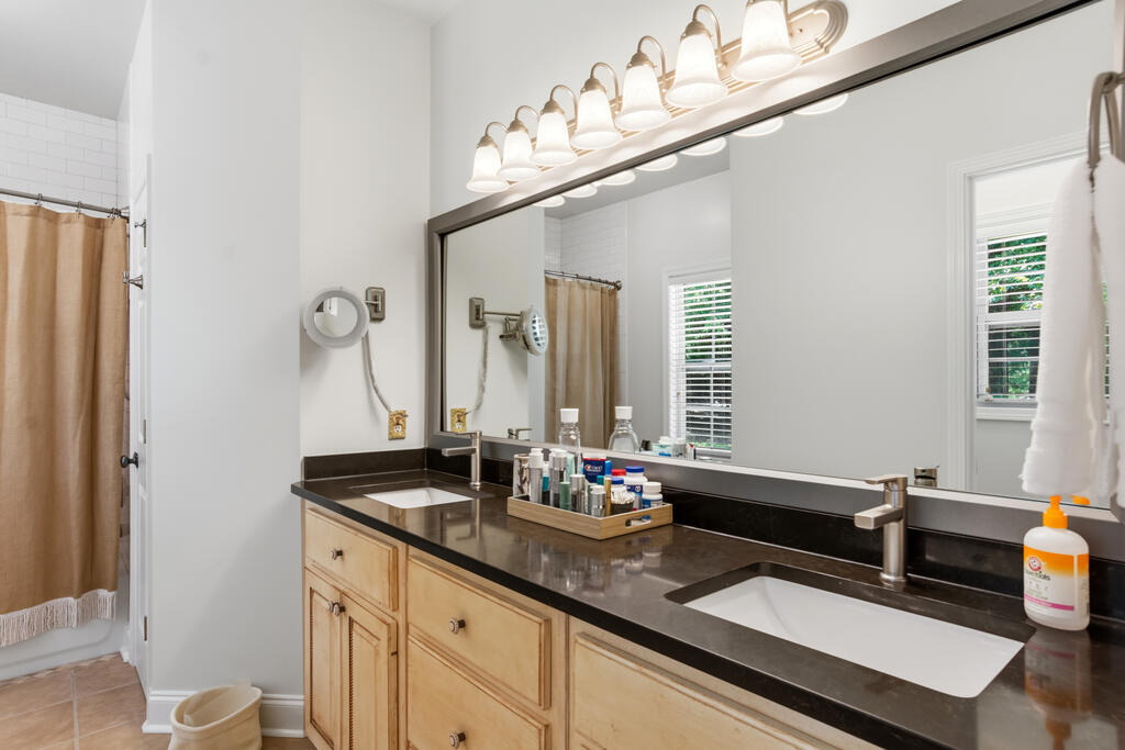 Bathroom vanity with a large mirror, bright lights, dark countertop, and tan shower curtain.