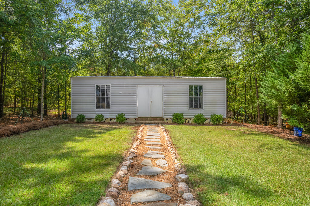 Single-story home with a stone-edged walkway through a grassy, wooded yard.