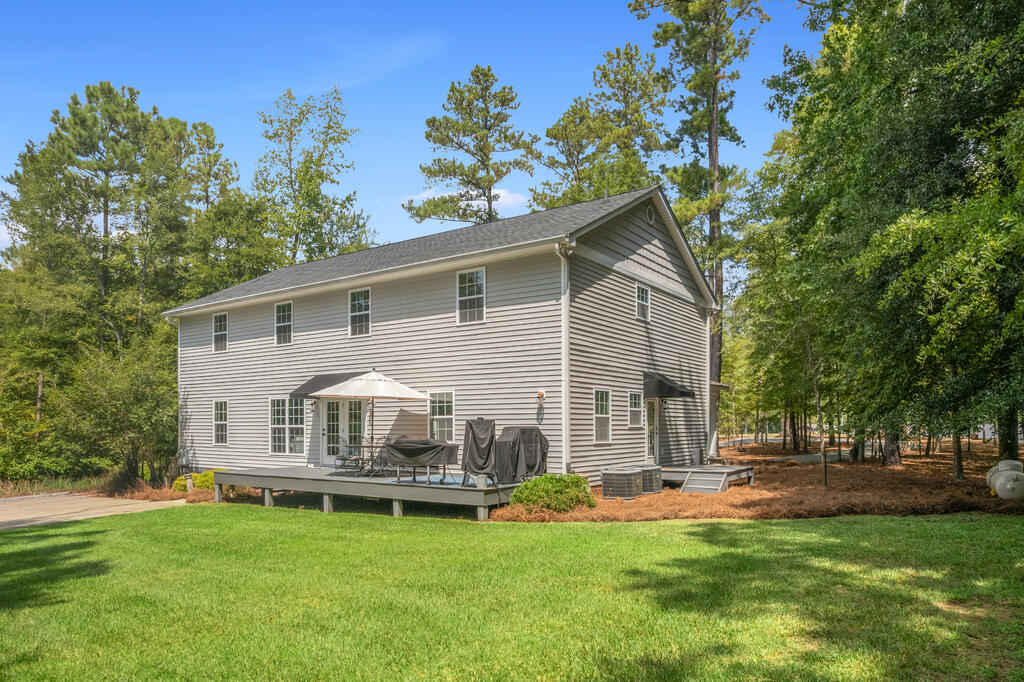 Two-story gray-sided house with a raised deck and green lawn, surrounded by trees.