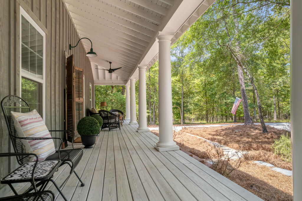 Covered porch with white columns and rocking chairs overlooking a wooded yard.