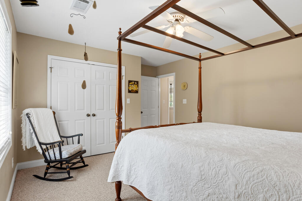 Furnished bedroom with a dark wood canopy bed, white quilt, and rocking chair beside the window.
